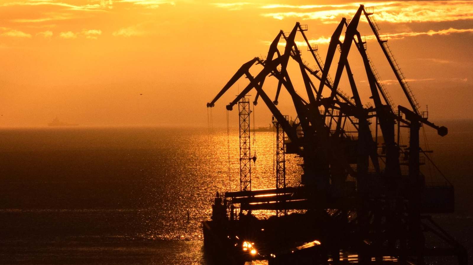 Port cranes silhouetted against a sunset over the water